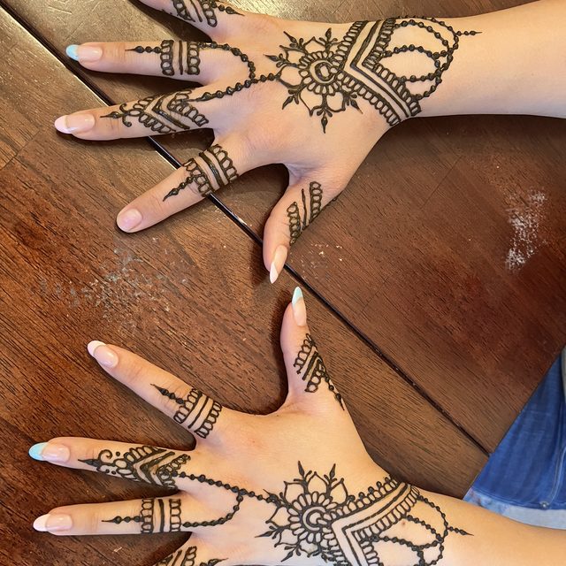 Lace-pattern henna on a pair of hands with rings