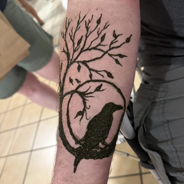 Tree and raven silhouette henna design on the forearm